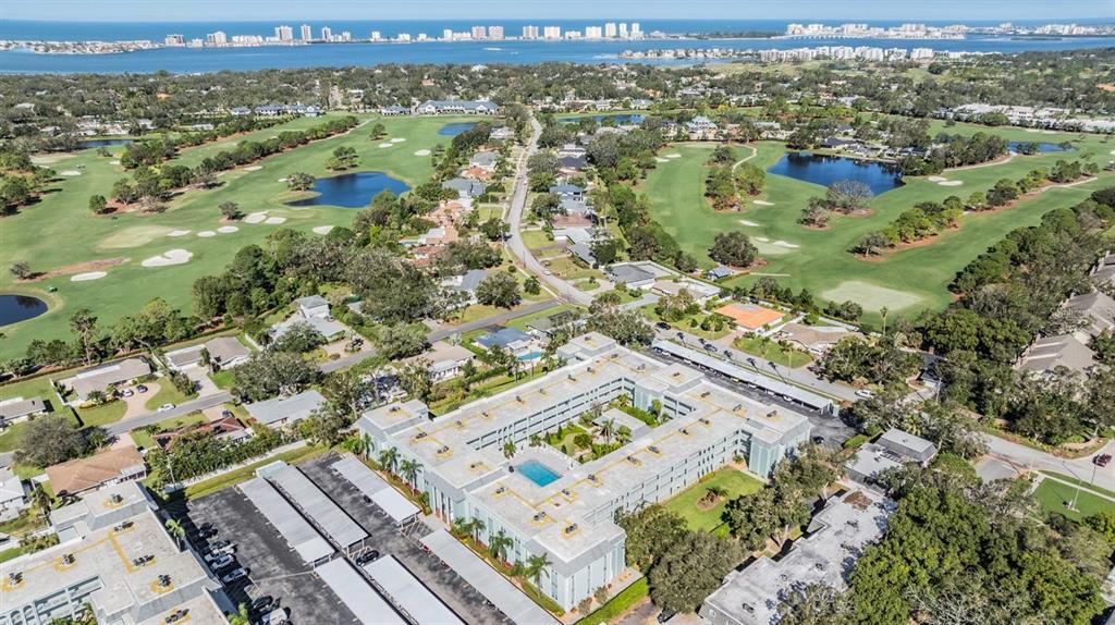 An aerial view shows a multi-story apartment complex with a pool, surrounded by golf courses — 1706 BELLEAIR FOREST DRIVE UNIT 136, CLEARWATER, FL