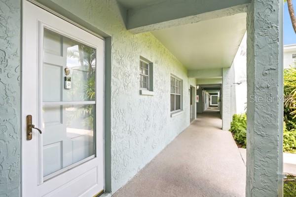 A white front door with a storm door opens onto a covered outdoor walkway — 1706 BELLEAIR FOREST DRIVE UNIT 136, CLEARWATER, FL