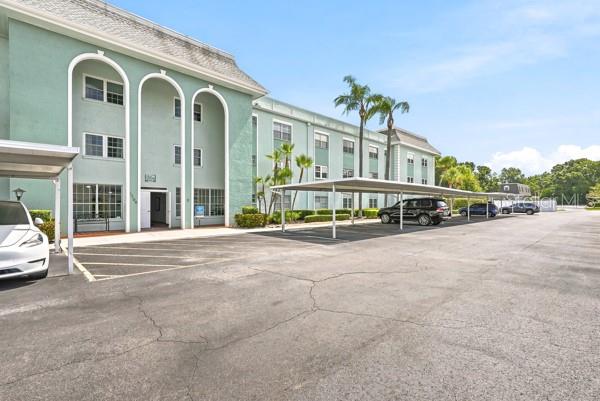 A multi-story light green apartment building features arched entryways and a covered parking area — 1706 BELLEAIR FOREST DRIVE UNIT 136, CLEARWATER, FL
