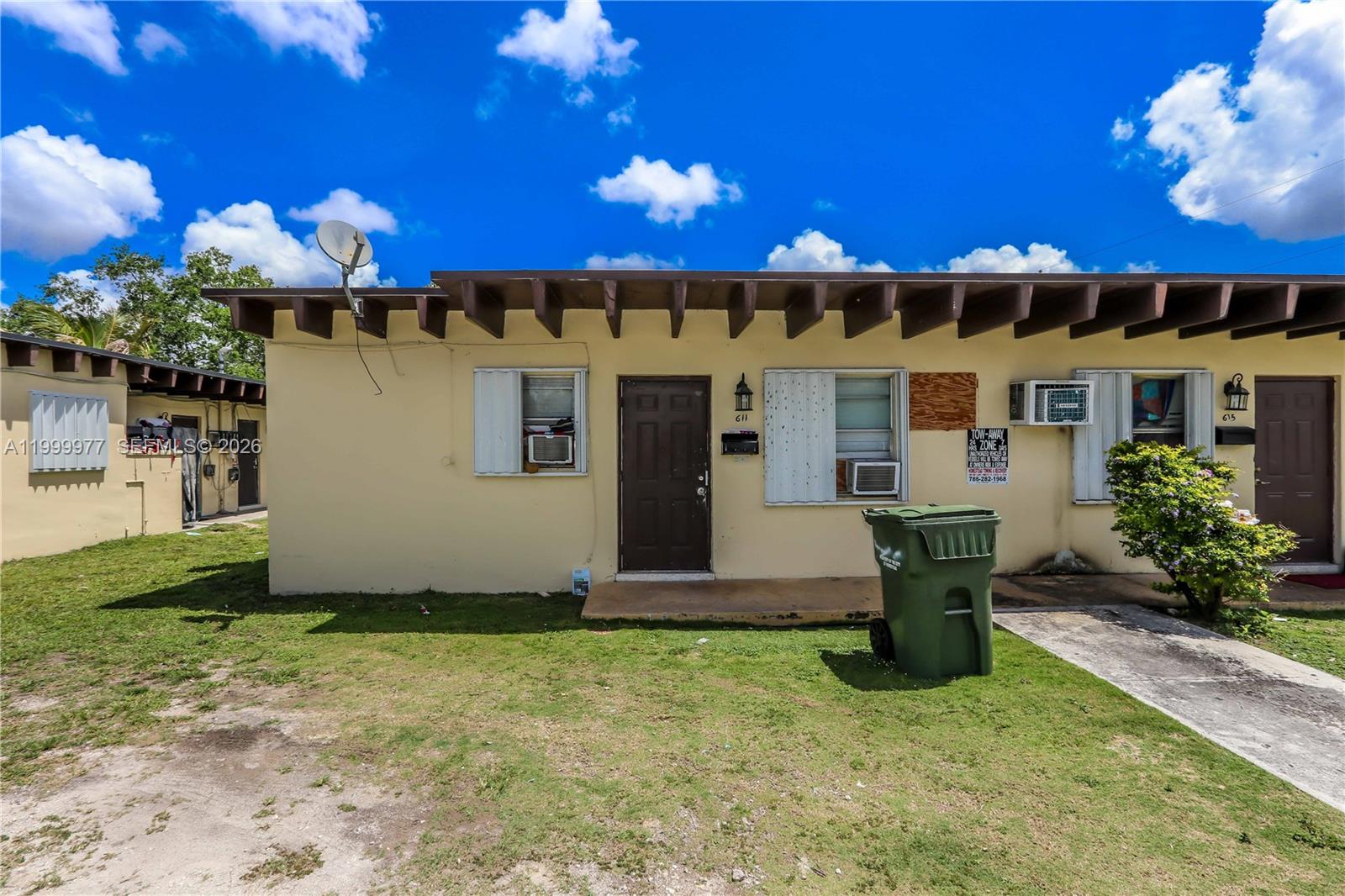 The exterior of a single-story, beige apartment building features a brown door and a trash bin — 611 SW 8th Ave, Homestead FL 33030, HOMESTEAD, FL