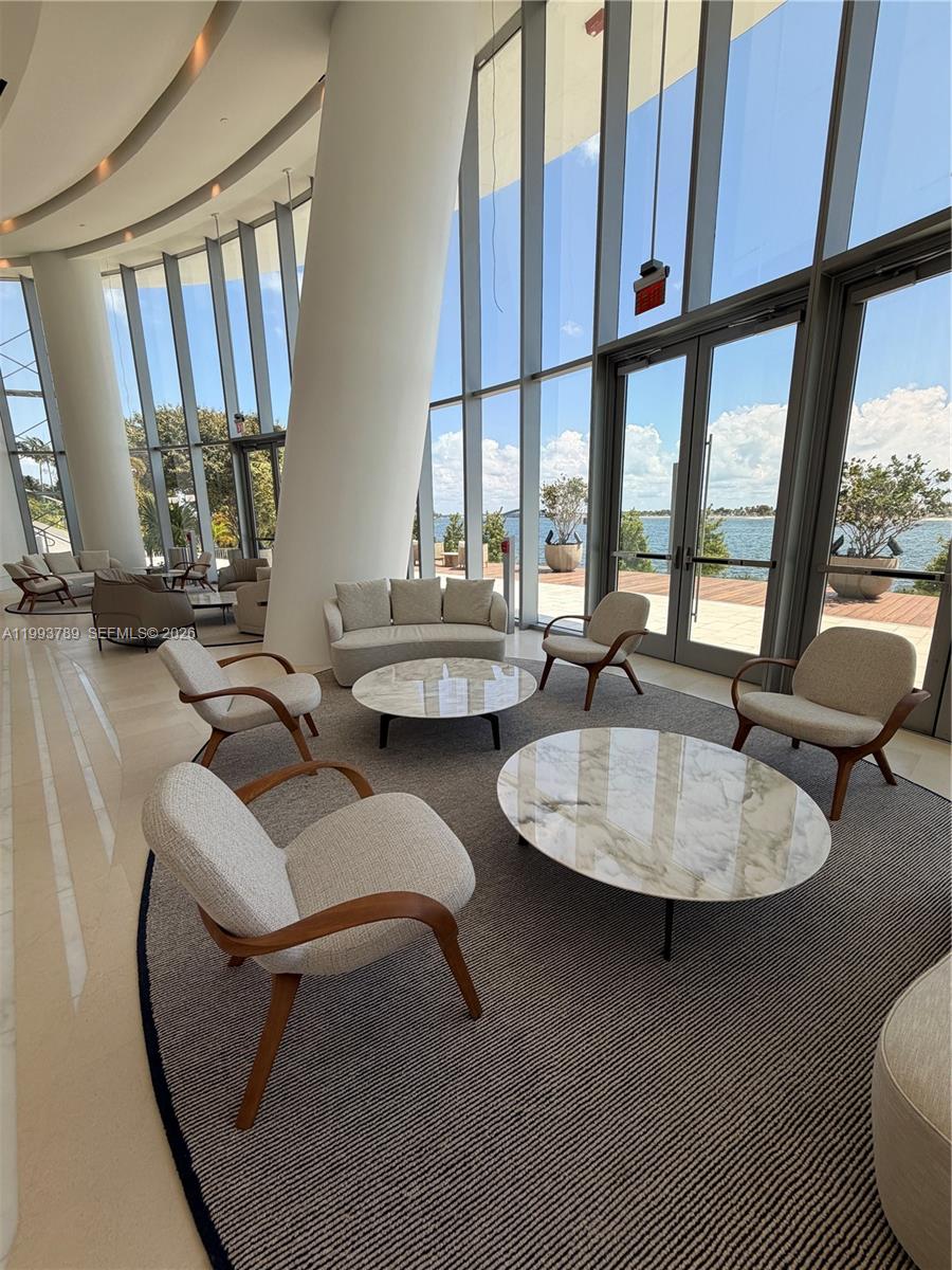 A modern lounge area features curved floor-to-ceiling windows overlooking a waterfront patio — 175 SE 25th Rd # 2101, Miami FL 33129, MIAMI, FL