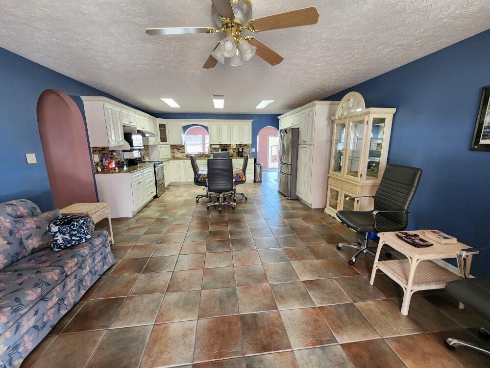 A kitchen and living area with blue walls, tile flooring, white cabinets, and a ceiling fan — 1177 Lisa Lane, Okeechobee FL 34974, OKEECHOBEE, FL