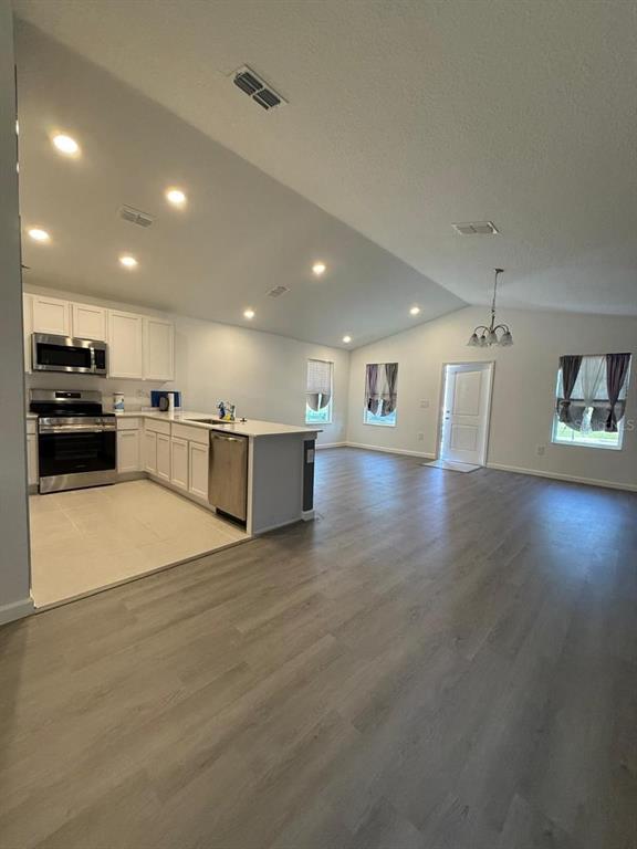 An open-concept kitchen and living area features white cabinetry, stainless steel appliances, and wood-look flooring — 1970 SARAH STREET, WINTER HAVEN, FL