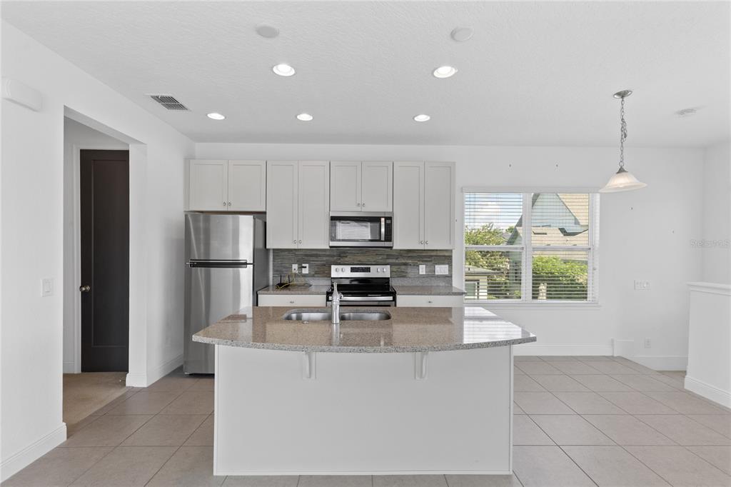 A kitchen features white cabinets, stainless steel appliances, a granite island, and tile flooring — 13153 LESSING AVENUE, ORLANDO, FL
