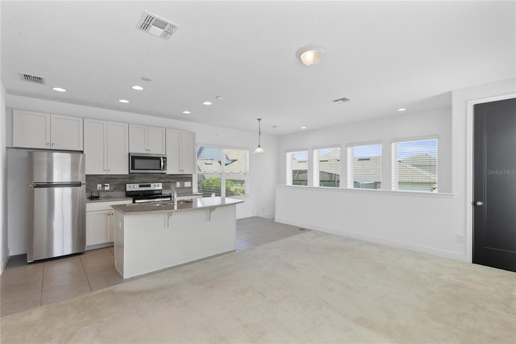 A kitchen with white cabinets and stainless steel appliances opens to a carpeted living area — 13153 LESSING AVENUE, ORLANDO, FL