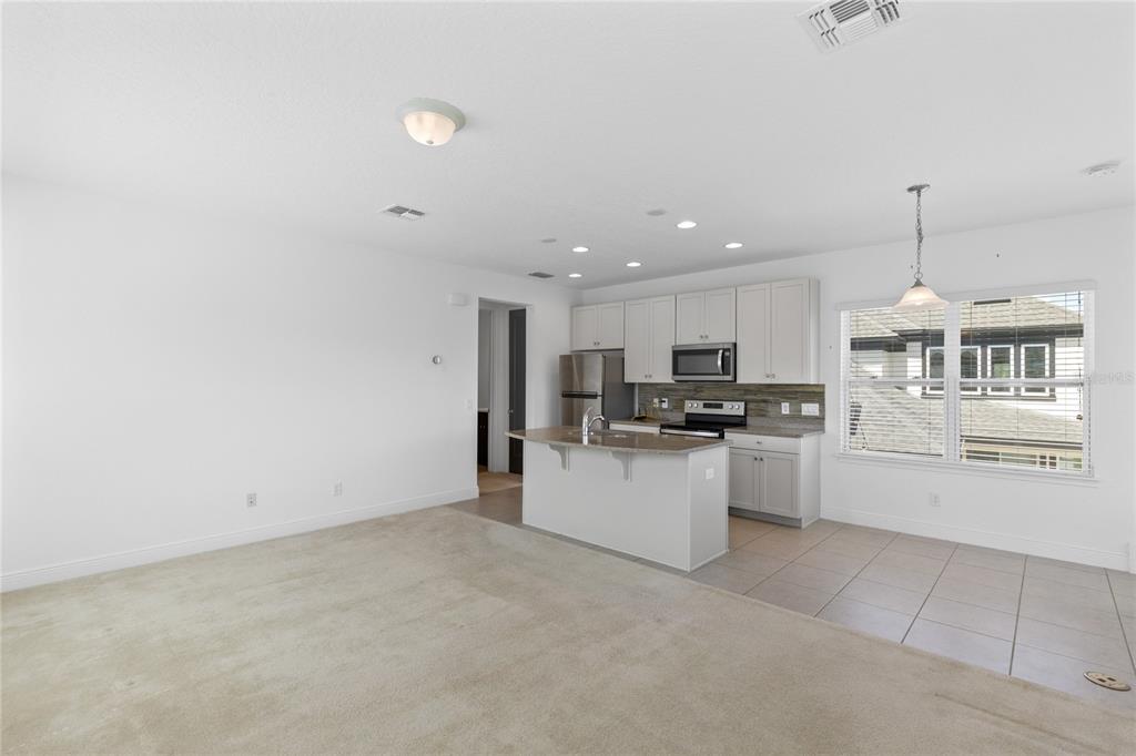 An open-concept kitchen with light gray cabinets and an island overlooks a carpeted living area — 13153 LESSING AVENUE, ORLANDO, FL