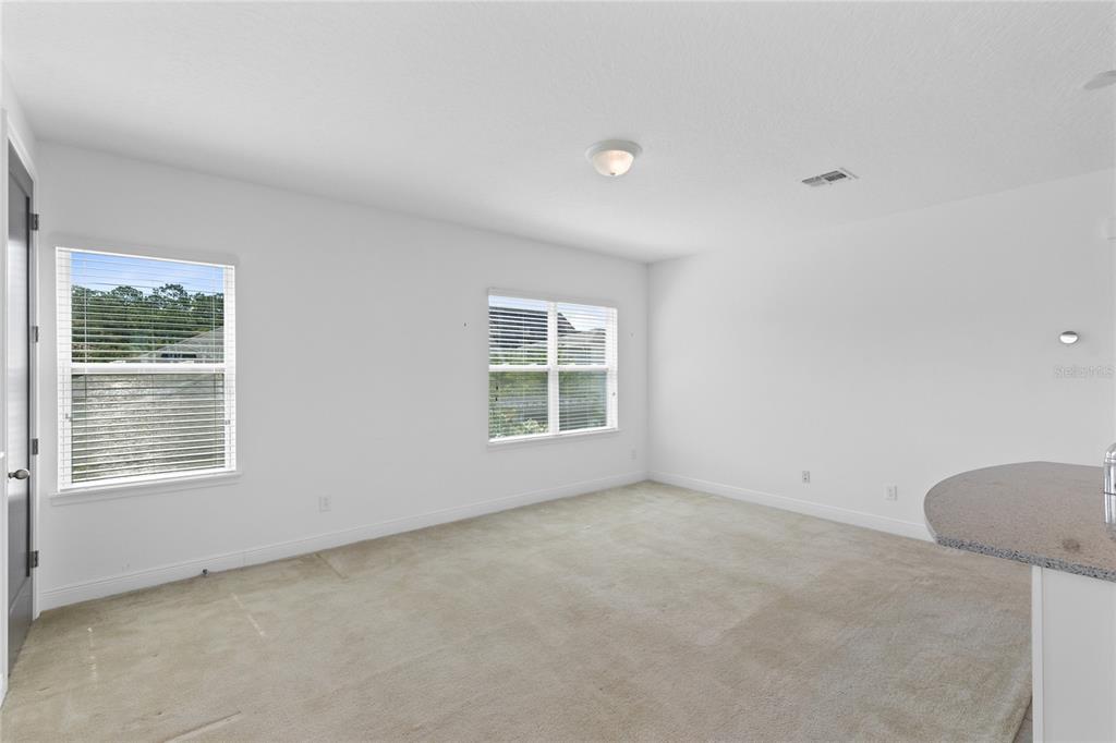An empty room with white walls, beige carpeting, two windows, and a partial kitchen counter — 13153 LESSING AVENUE, ORLANDO, FL