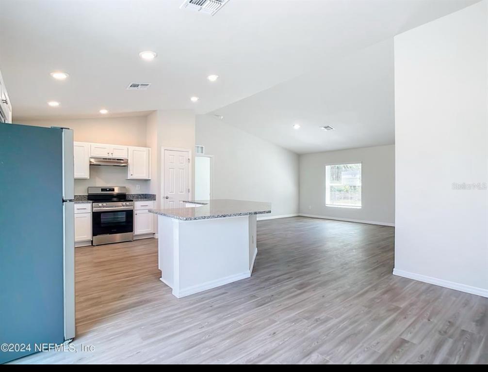 An open-concept kitchen and living area features white cabinets, granite countertops, and wood-look flooring — 315 MARION OAKS CRSE ROAD, OCALA, FL