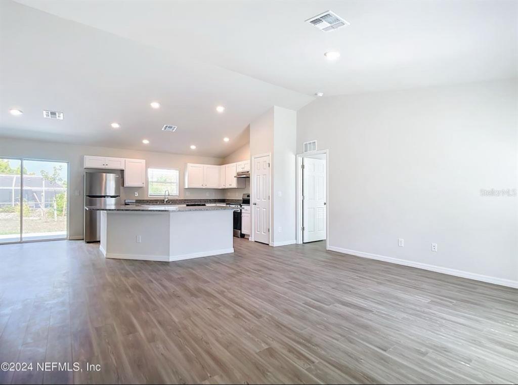 An open-concept kitchen with white cabinets and a granite island overlooks a living area — 315 MARION OAKS CRSE ROAD, OCALA, FL