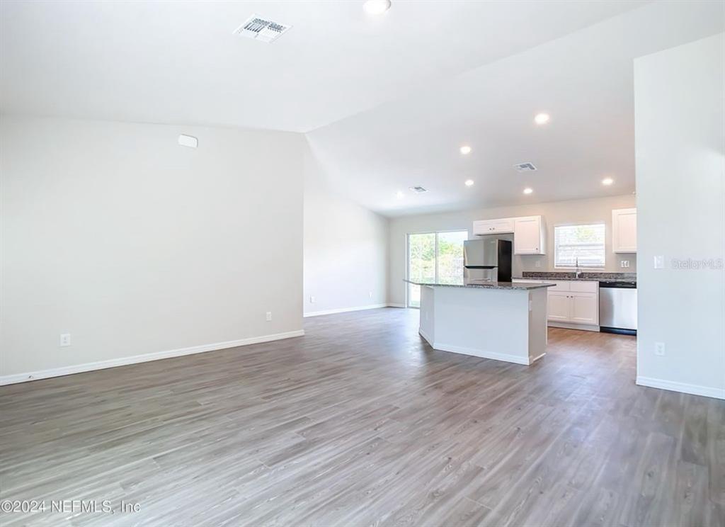 An open-concept living area features light wood-look flooring, a kitchen island, and white cabinetry — 315 MARION OAKS CRSE ROAD, OCALA, FL