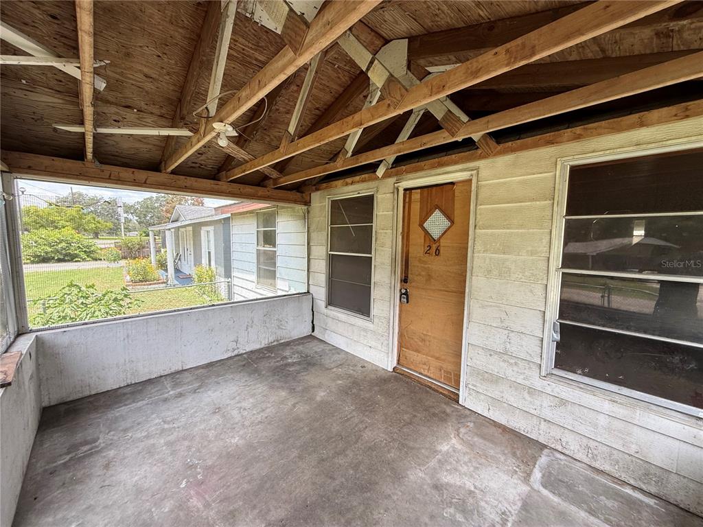 A covered porch features a concrete floor, exposed wooden rafters, and a wooden front door — 26 ATLANTIC AVENUE, MASCOTTE, FL