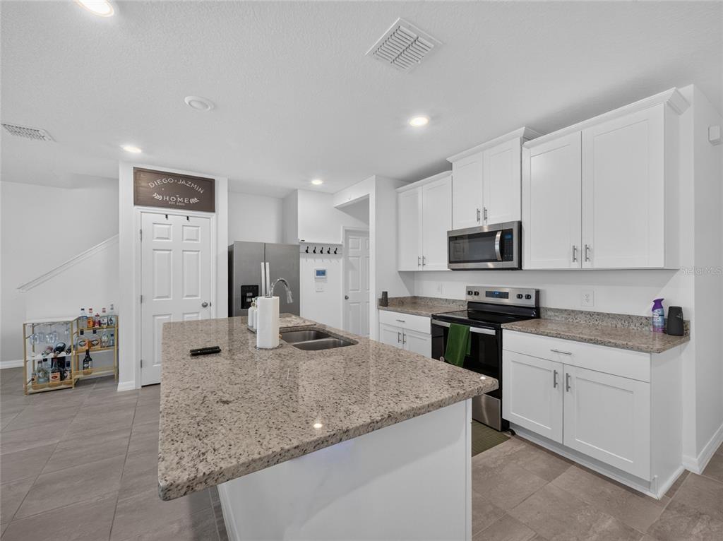 A kitchen features white cabinets, granite countertops, a central island, and stainless steel appliances — 4368 RANCH HOUSE ROAD, ST CLOUD, FL