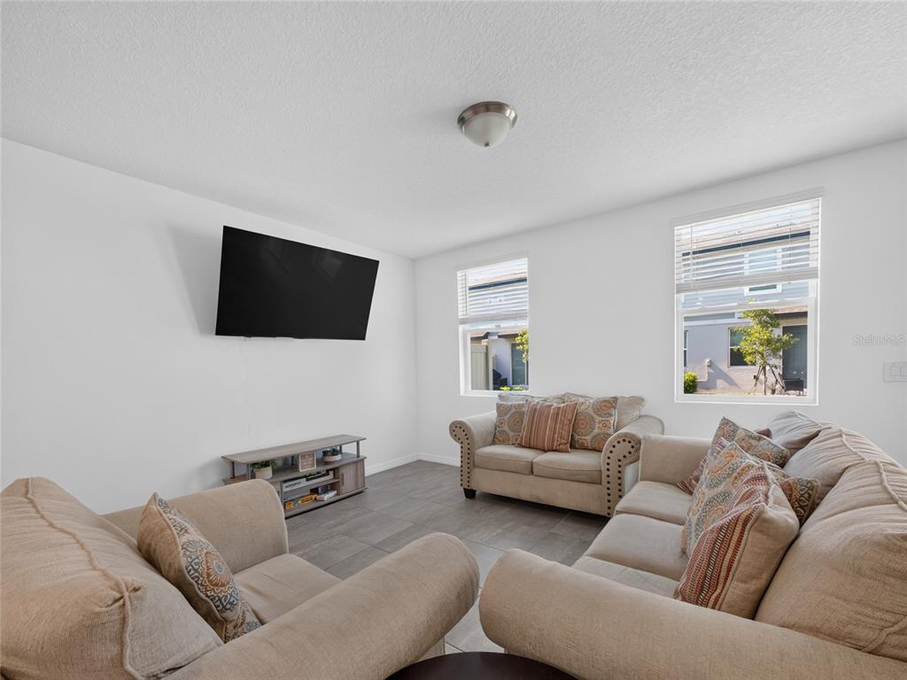 A living room features a wall-mounted television, a media console, and beige upholstered furniture — 4368 RANCH HOUSE ROAD, ST CLOUD, FL