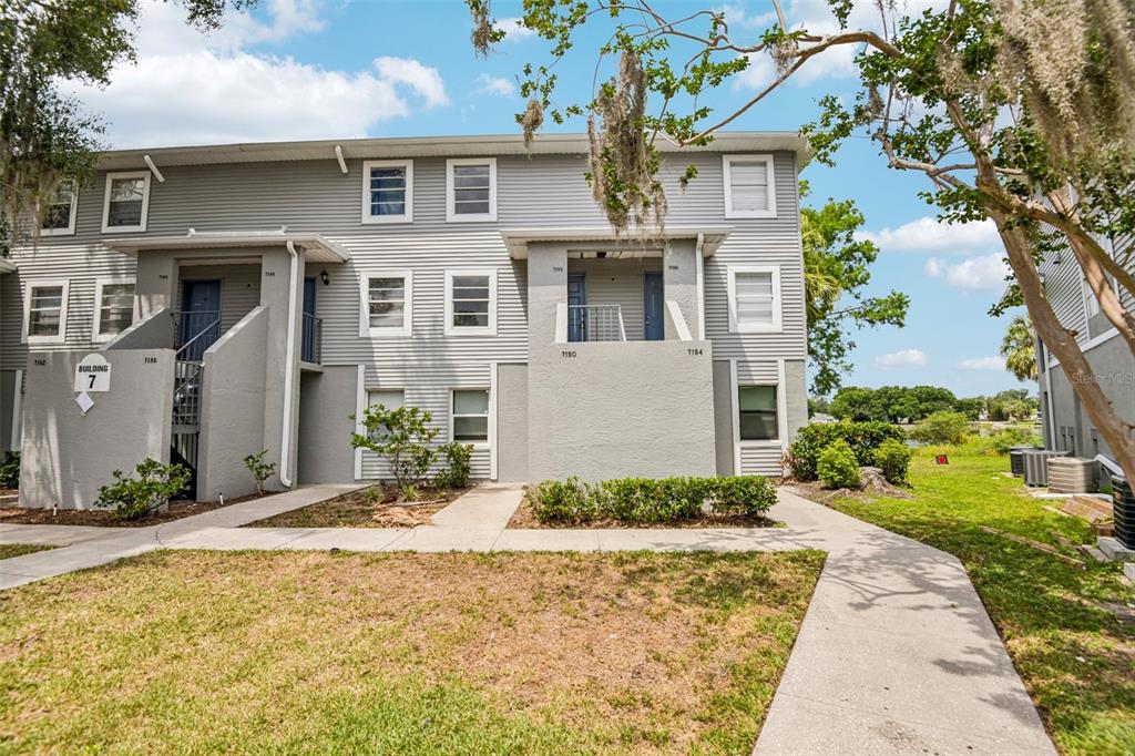 A three-story apartment building with gray siding and concrete walkways in front — 7192 E BANK DRIVE UNIT 7192, TAMPA, FL