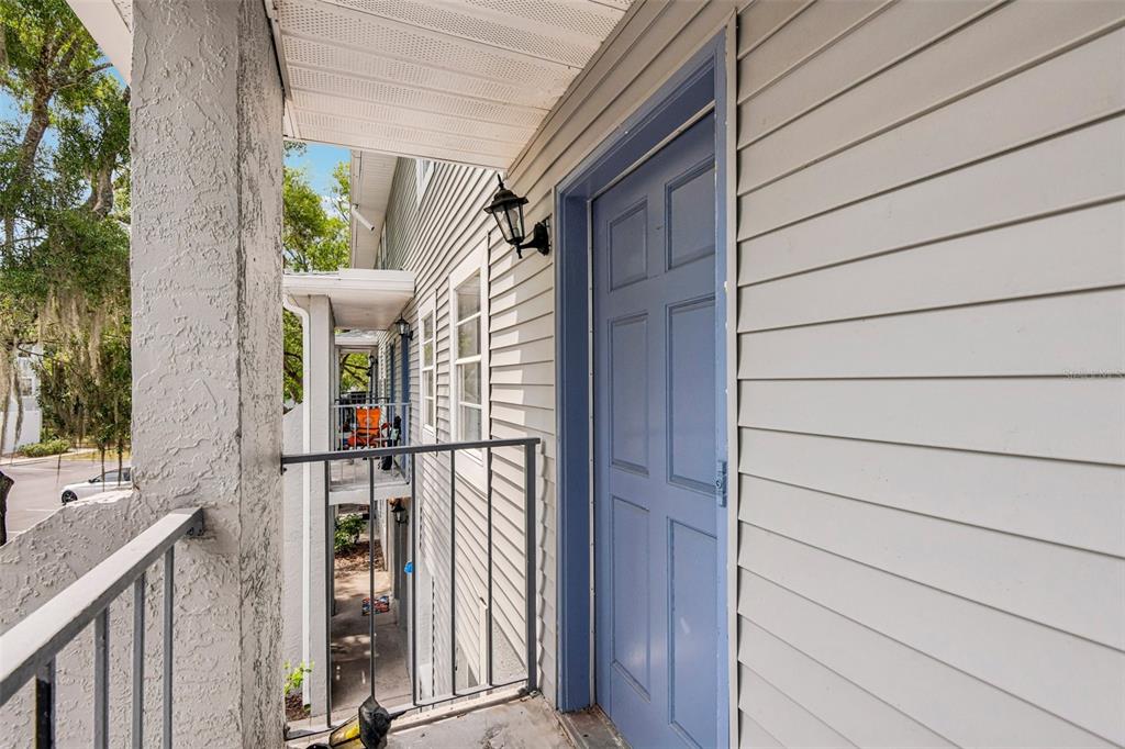 A blue door opens onto a covered balcony with gray siding and a metal railing — 7192 E BANK DRIVE UNIT 7192, TAMPA, FL