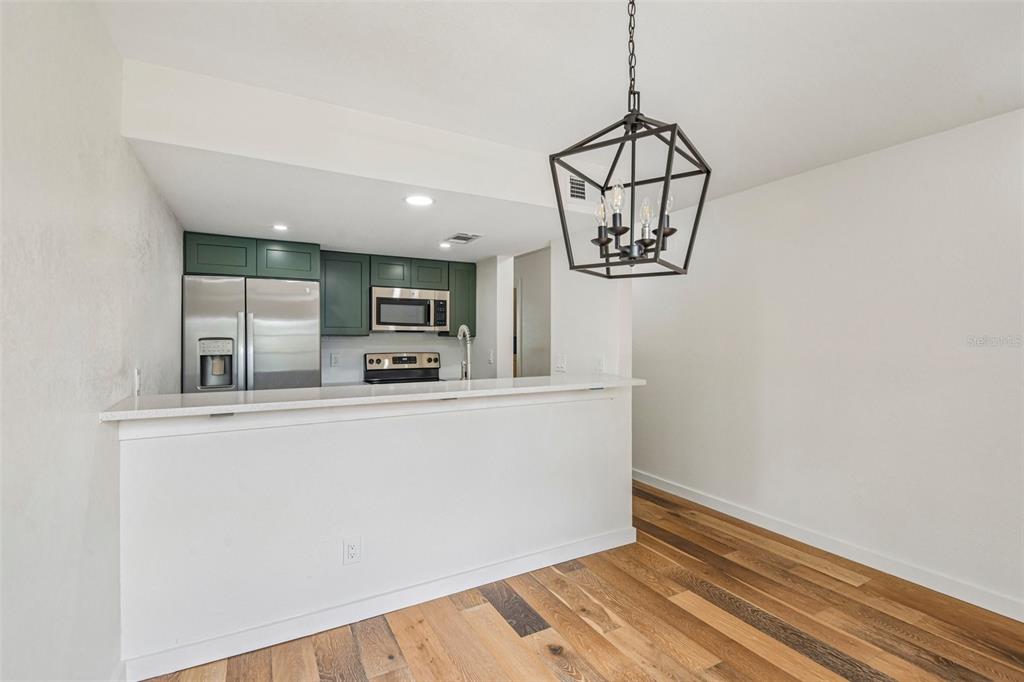 A kitchen with green cabinets and stainless steel appliances overlooks a dining area with wood flooring — 7192 E BANK DRIVE UNIT 7192, TAMPA, FL