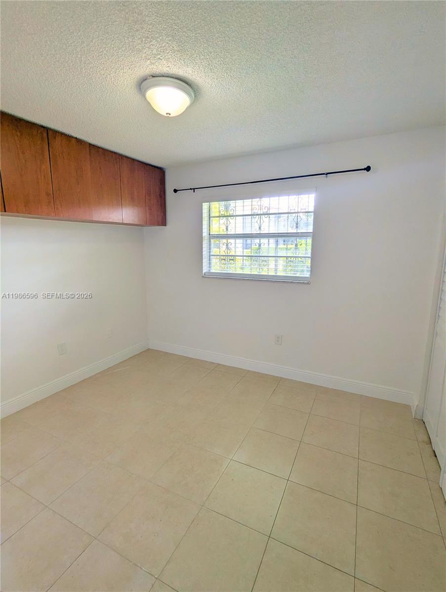A bedroom features light-colored tile flooring, white walls, a ceiling light, and overhead wooden cabinets — 4050 NW 135th St # 9, Opa-Locka FL 33054, OPA-LOCKA, FL