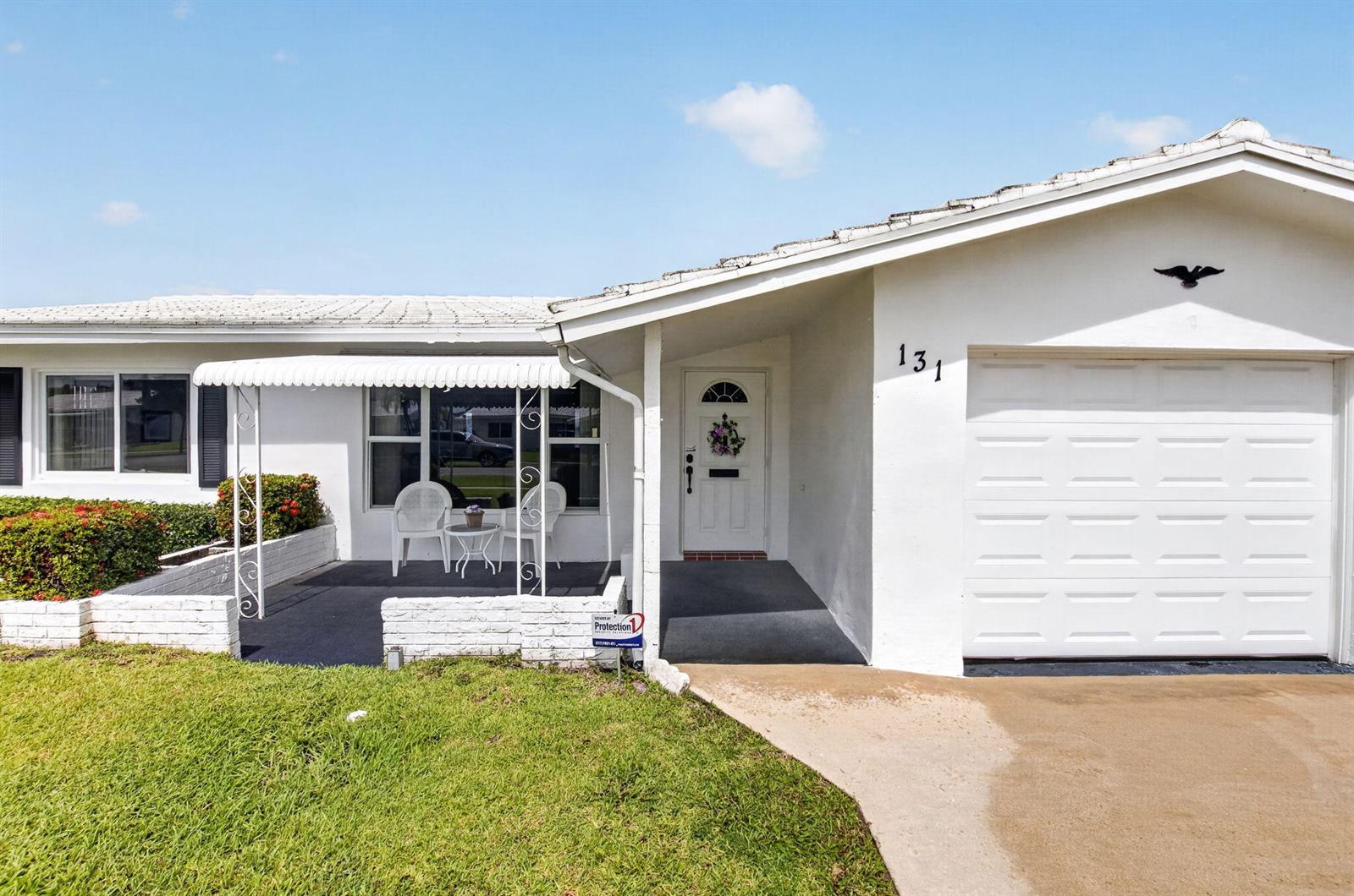 A white single-story house features a covered patio, a garage, and a small front lawn — 131 Leisureville Boulevard, Boynton Beach FL 33426, BOYNTON BEACH, FL