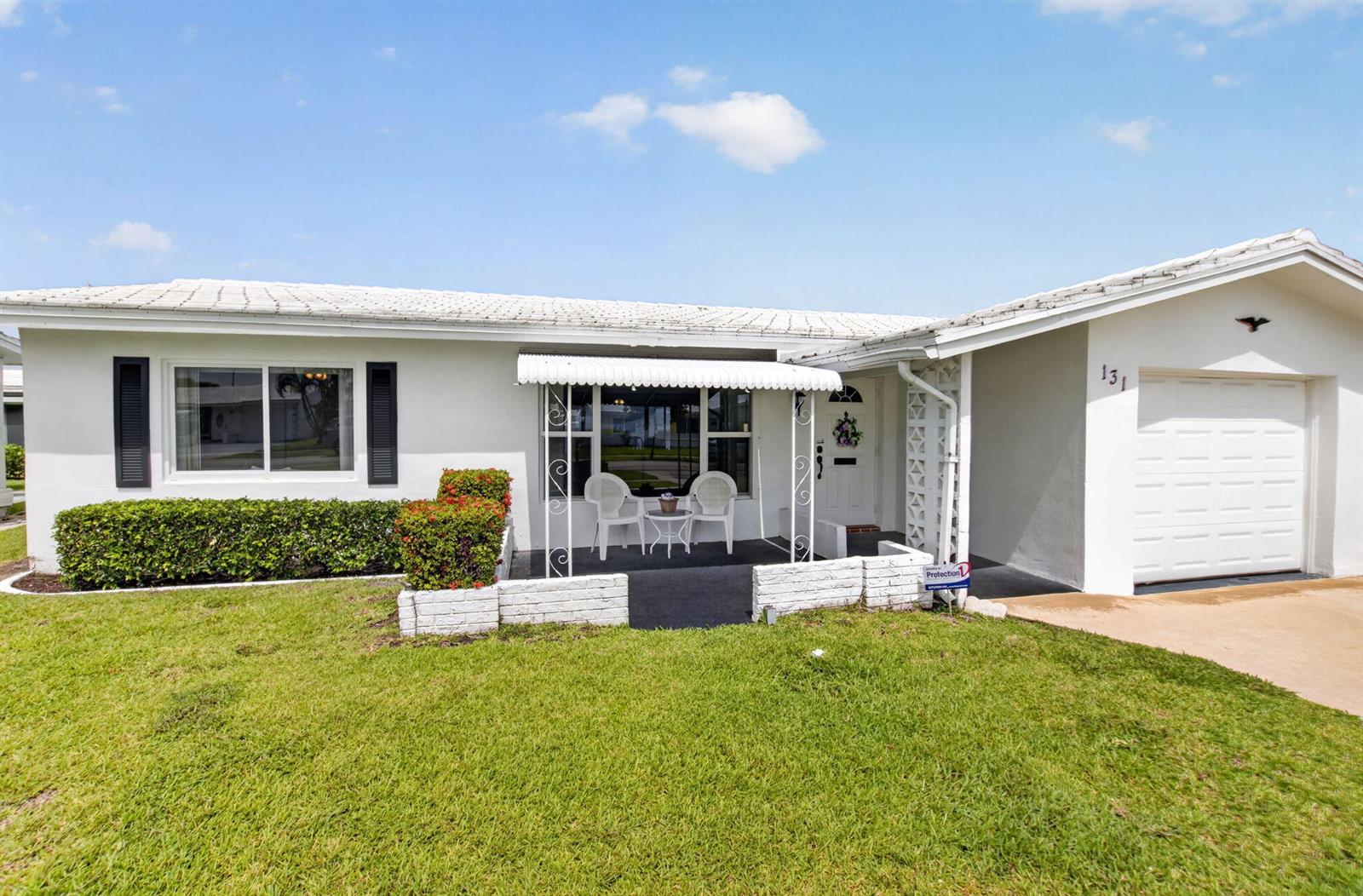 A white single-story house features a front porch, a garage, and a manicured lawn — 131 Leisureville Boulevard, Boynton Beach FL 33426, BOYNTON BEACH, FL