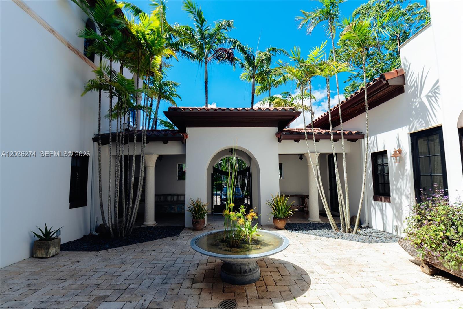 A courtyard features a stone fountain, palm trees, and white stucco walls under a blue sky — 6220 SW 86th St # 0, Miami FL 33143, MIAMI, FL