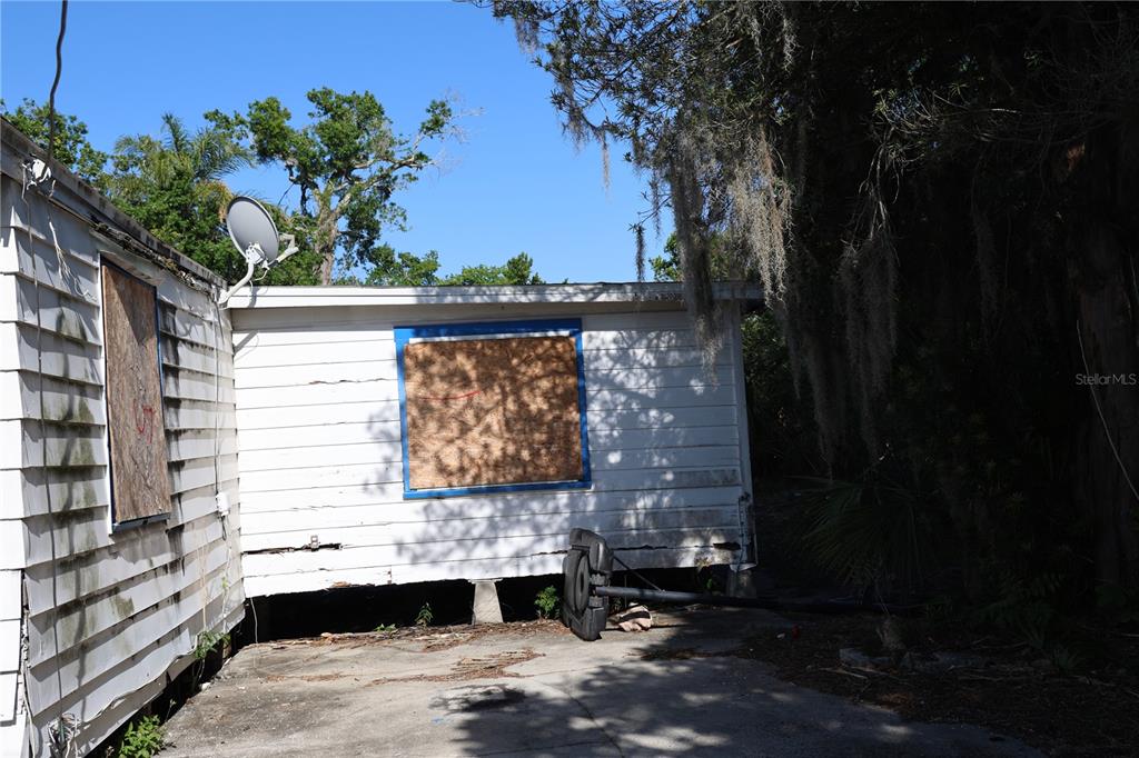 The exterior of a weathered, white-sided house features boarded-up windows and a satellite dish — 232 C STREET, LAKE WALES, FL