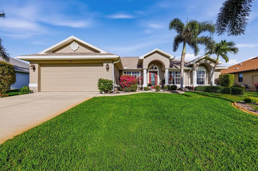 A single-story suburban house with a two-car garage, palm trees, and a green lawn — 827 ROTONDA CIRCLE, ROTONDA WEST, FL