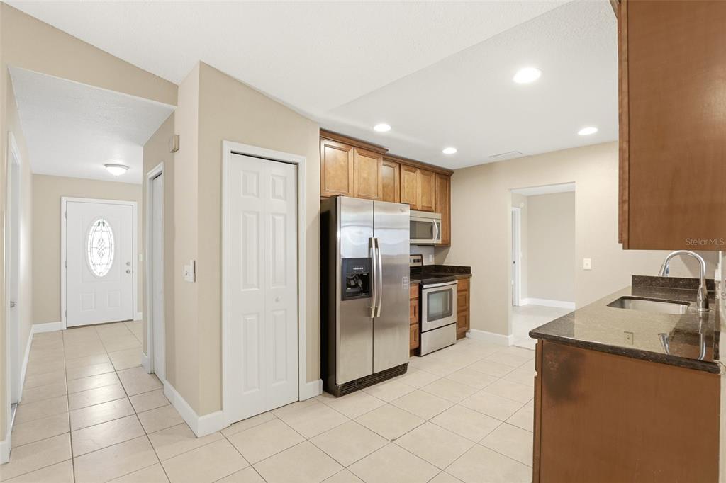 A kitchen with stainless steel appliances, wood cabinets, and tile flooring opens to an entryway — 7320 WETHERSFIELD DRIVE, ORLANDO, FL