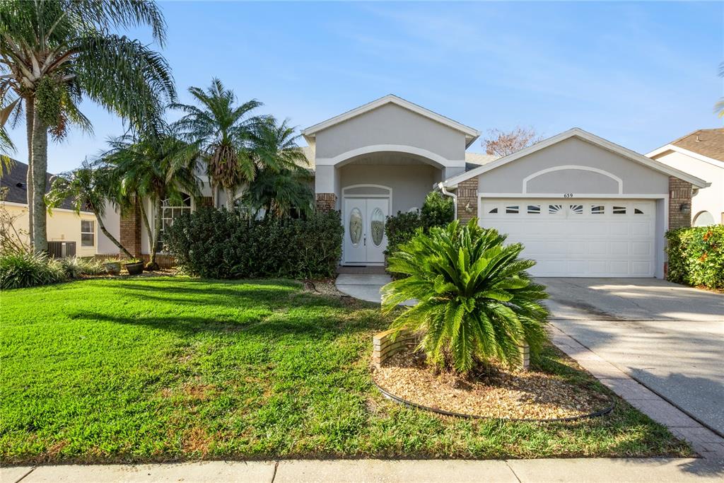 A single-story house with a white garage, arched entryway, and palm trees in the front yard — 639 LAKEHAVEN CIRCLE, ORLANDO, FL