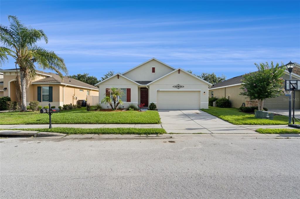 A single-story suburban house with a two-car garage, tan stucco exterior, and a front lawn — 1844 SKYVIEW DRIVE, AUBURNDALE, FL