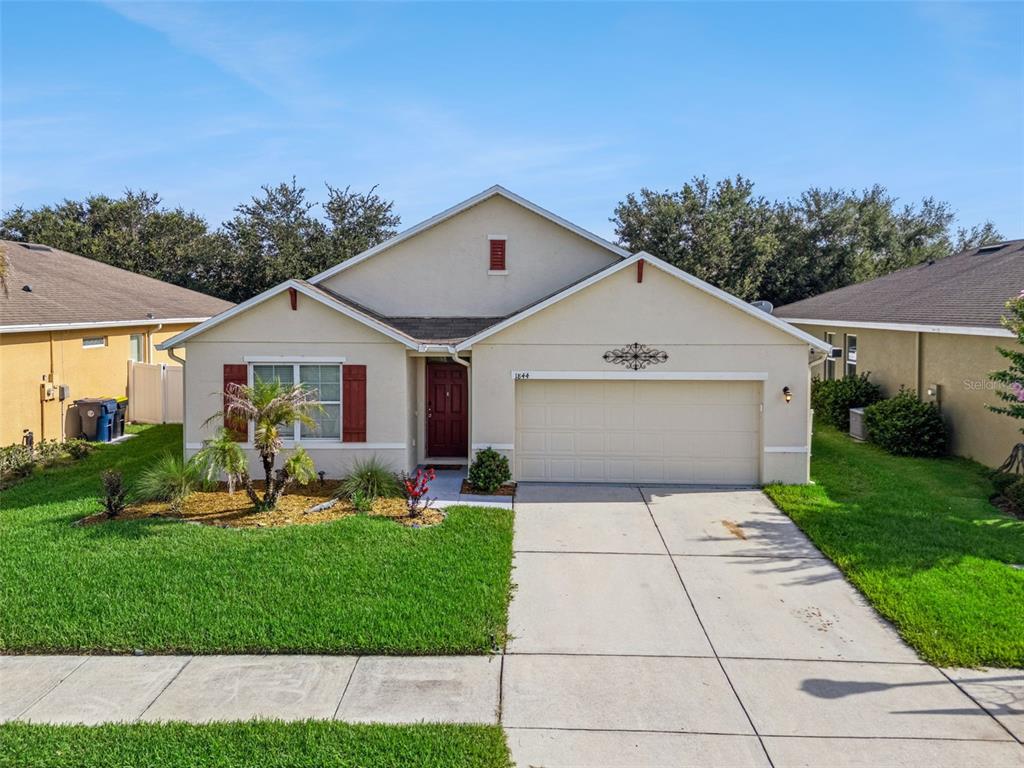 A single-story suburban house with a beige stucco exterior, a two-car garage, and a lawn — 1844 SKYVIEW DRIVE, AUBURNDALE, FL