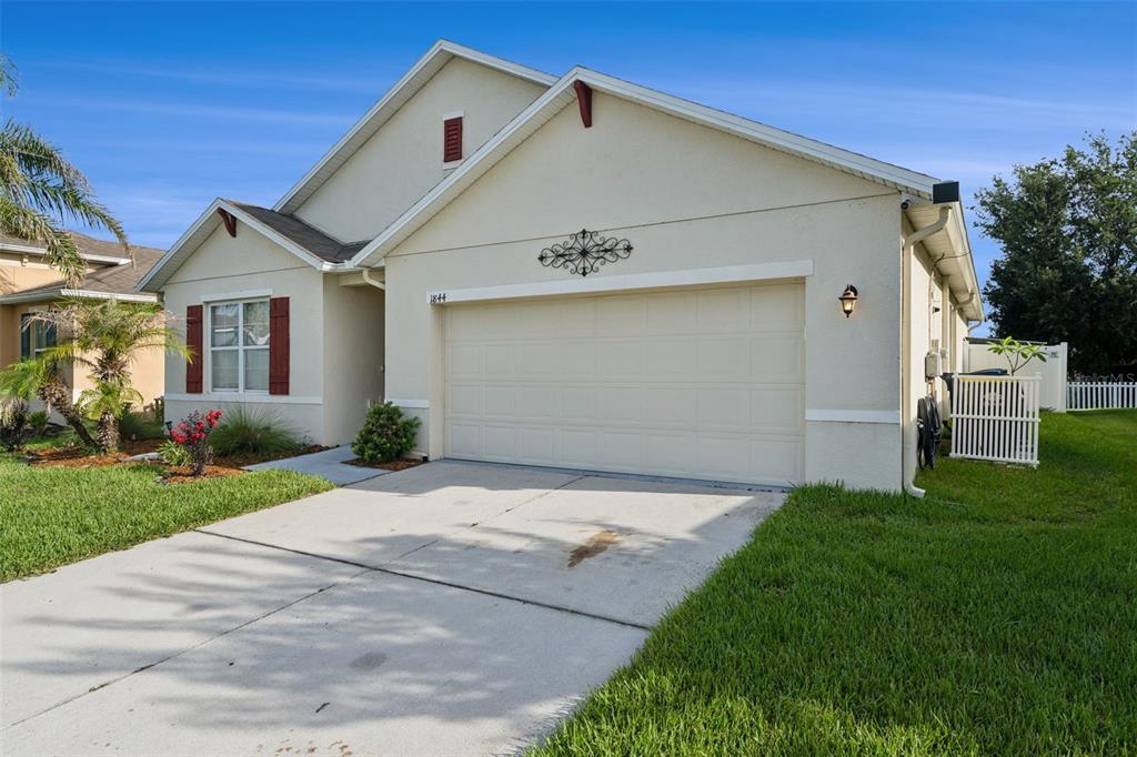 A single-story house with a beige stucco exterior, a two-car garage, and a concrete driveway — 1844 SKYVIEW DRIVE, AUBURNDALE, FL