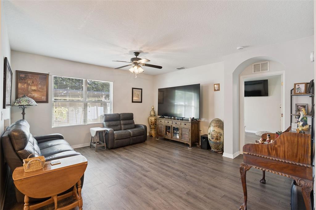 A living room with gray wood-look flooring, a ceiling fan, and a large television console — 1844 SKYVIEW DRIVE, AUBURNDALE, FL