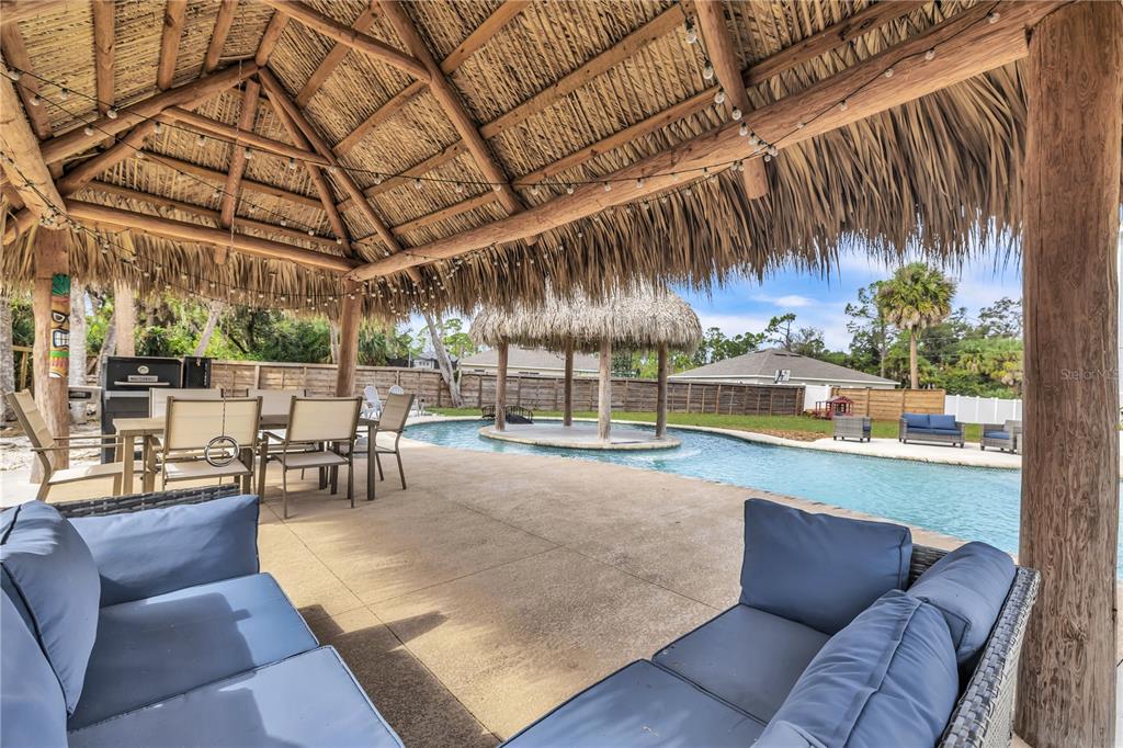 A covered patio with a thatched roof overlooks a swimming pool with a tiki hut island — 3694 CRANDON ROAD, NORTH PORT, FL