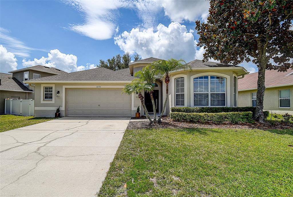 A single-story suburban house with a two-car garage, palm tree, and arched windows — 16730 FAIRBOLT WAY, ODESSA, FL
