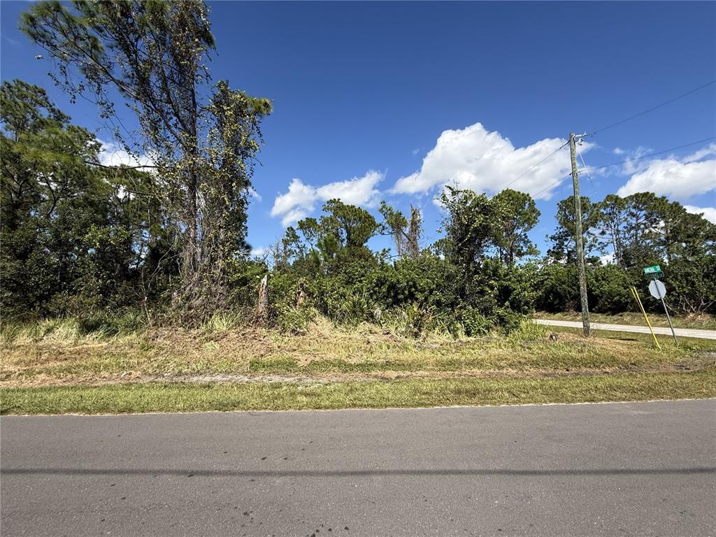 A vacant, wooded lot sits at a street corner under a clear blue sky — 7538 BERNAL DRIVE, SEBRING, FL