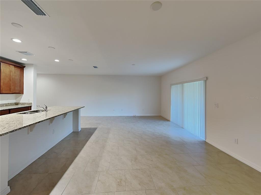 An open-concept kitchen with a granite island overlooks a spacious living area with tile floors — 1615 CLOUDY COURT, ST CLOUD, FL