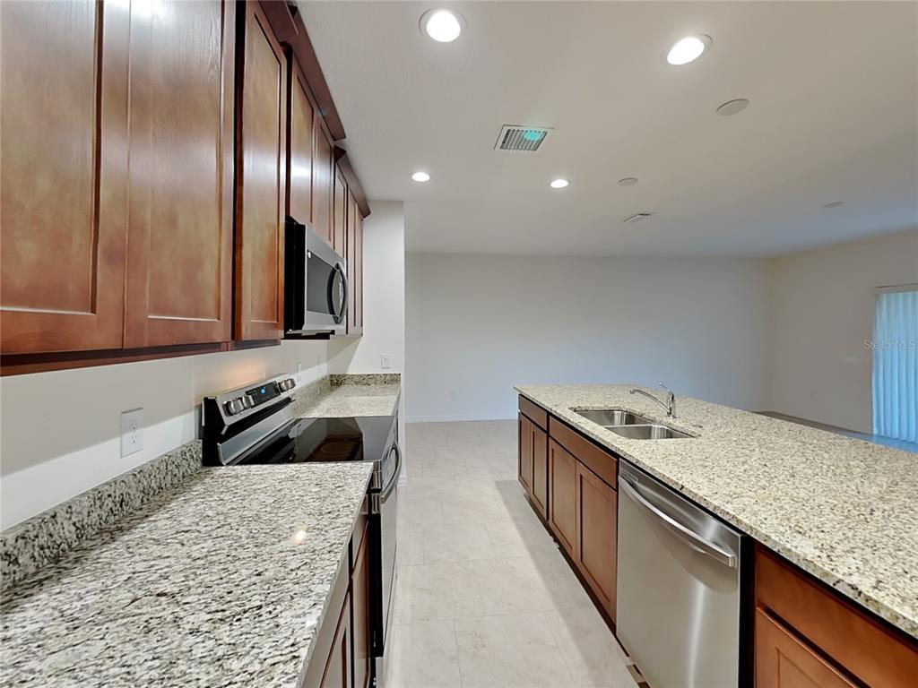 A kitchen features dark wood cabinets, granite countertops, stainless steel appliances, and tile flooring — 1615 CLOUDY COURT, ST CLOUD, FL