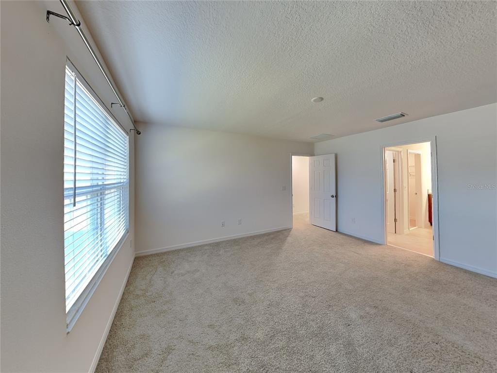 An empty bedroom features beige carpeting, white walls, a window with blinds, and two doorways — 1615 CLOUDY COURT, ST CLOUD, FL
