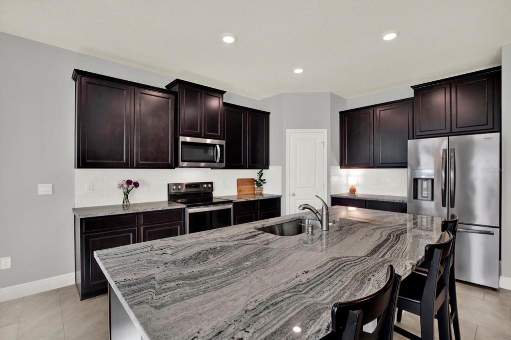 A kitchen features dark wood cabinets, stainless steel appliances, and a large granite-topped island — 32332 ROSEPINE BOULEVARD, WESLEY CHAPEL, FL