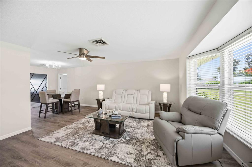 A living room with wood-look flooring, a white sofa, a grey recliner, and a dining area — 1933 FAIRVIEW DRIVE, ENGLEWOOD, FL