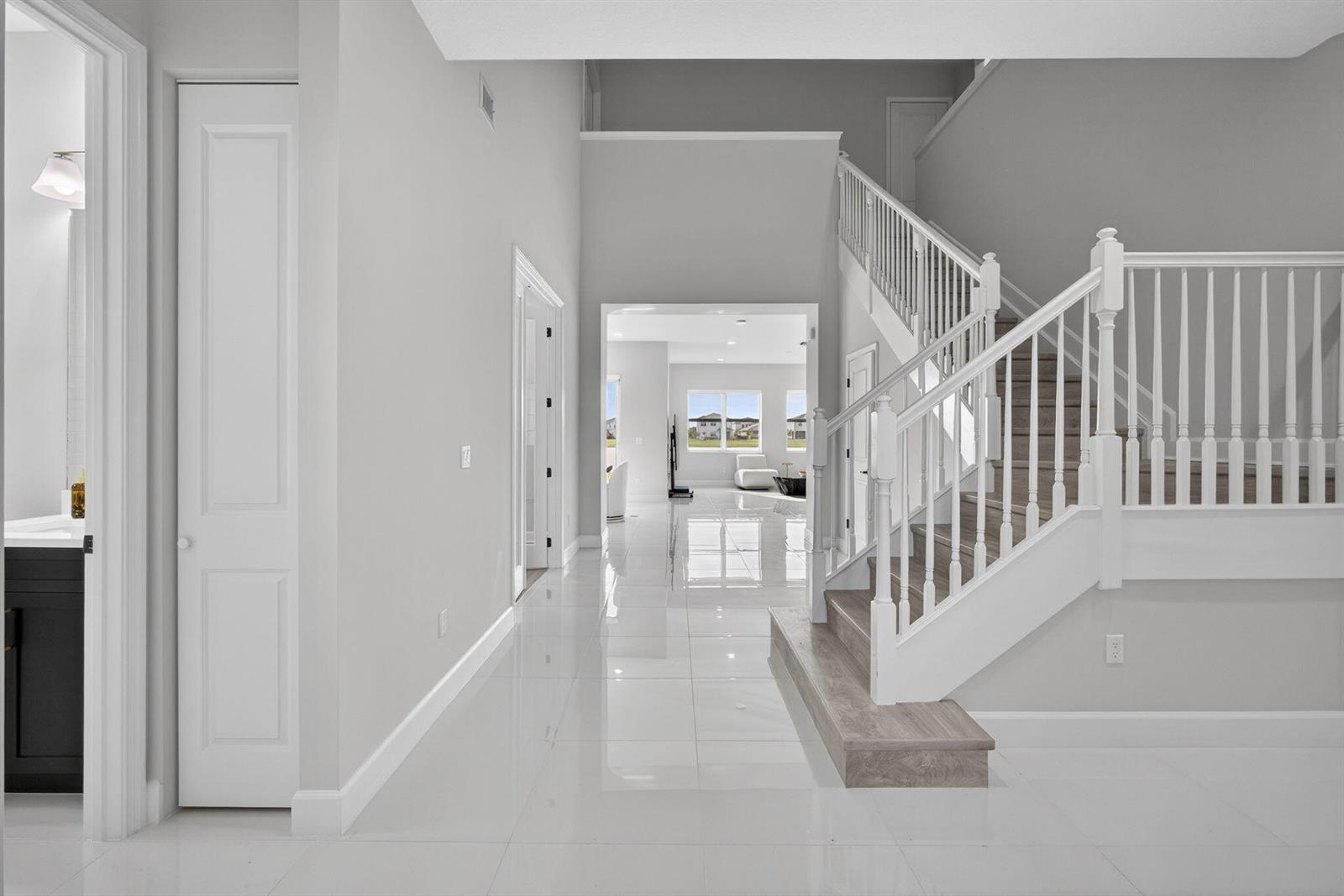 A bright foyer features white tile floors, a staircase with wooden treads, and neutral walls — 14052 Spruce Pine Drive, FL 33470, FL