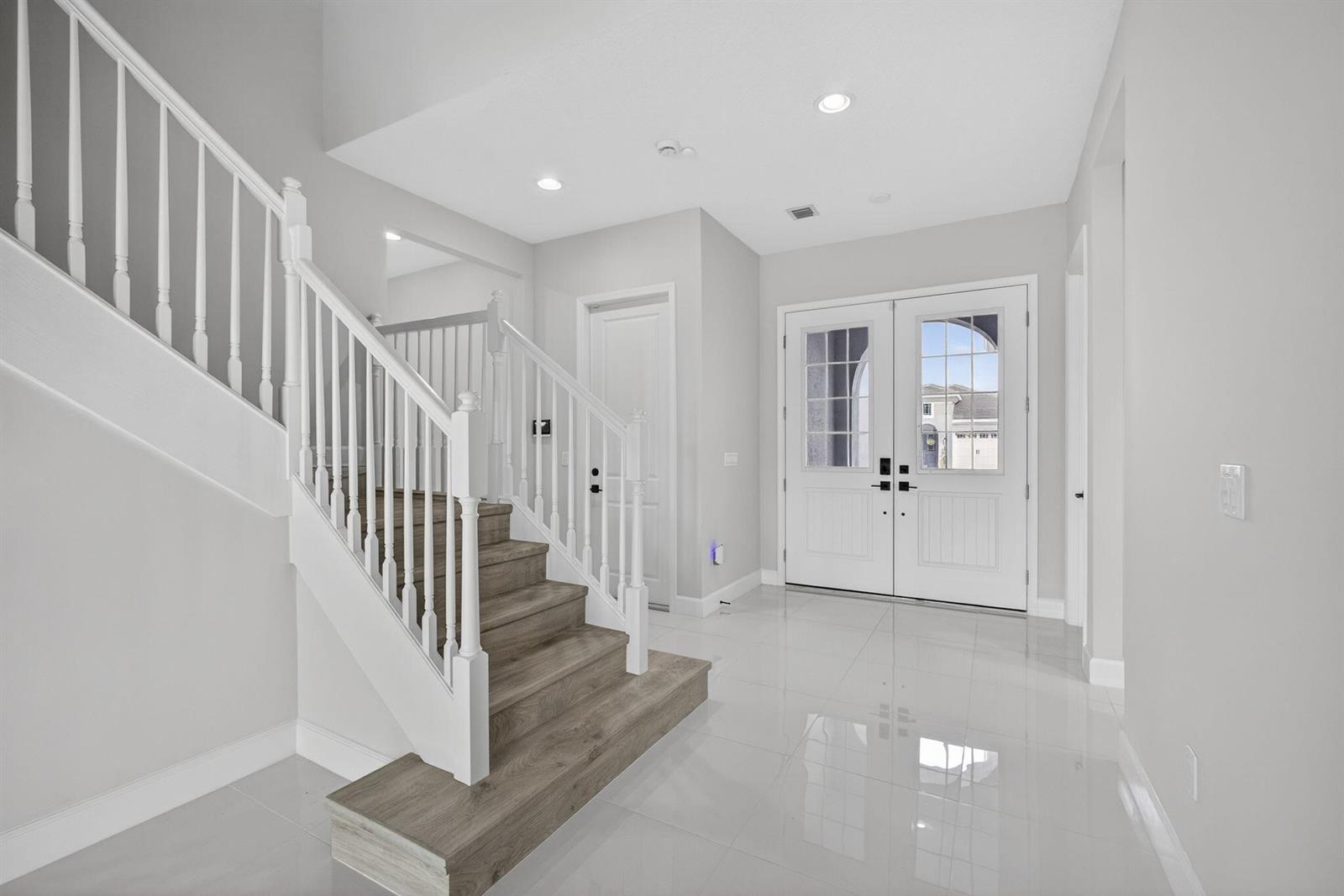 A bright entryway features white tile floors, a wooden staircase, and double front doors — 14052 Spruce Pine Drive, FL 33470, FL
