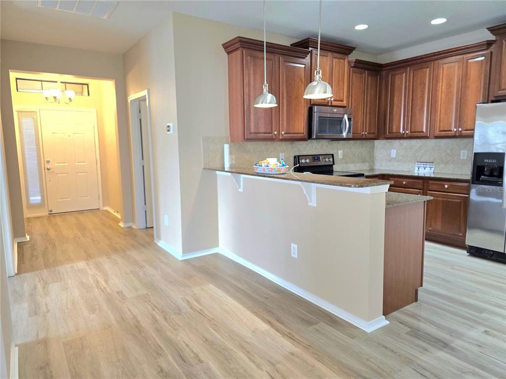 A kitchen features wood cabinets, granite countertops, and a breakfast bar overlooking a hallway — 5646 SUNSET FALLS DRIVE, APOLLO BEACH, FL