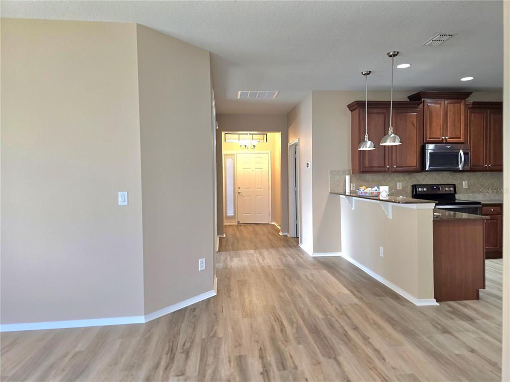 An open-concept interior features wood-look flooring, a kitchen with dark cabinets, and a front entryway — 5646 SUNSET FALLS DRIVE, APOLLO BEACH, FL