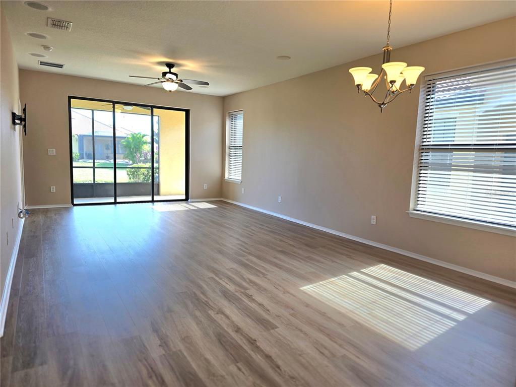 An open-concept living and dining area features light wood-look flooring and a kitchen in back — 5646 SUNSET FALLS DRIVE, APOLLO BEACH, FL