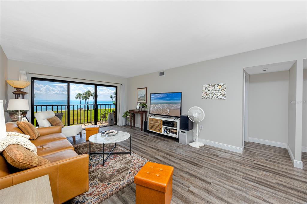 A living room features wood-look flooring, a leather sofa, and a sliding glass door overlooking water — 7530 SUNSHINE SKYWAY LANE S UNIT 115, ST PETERSBURG, FL