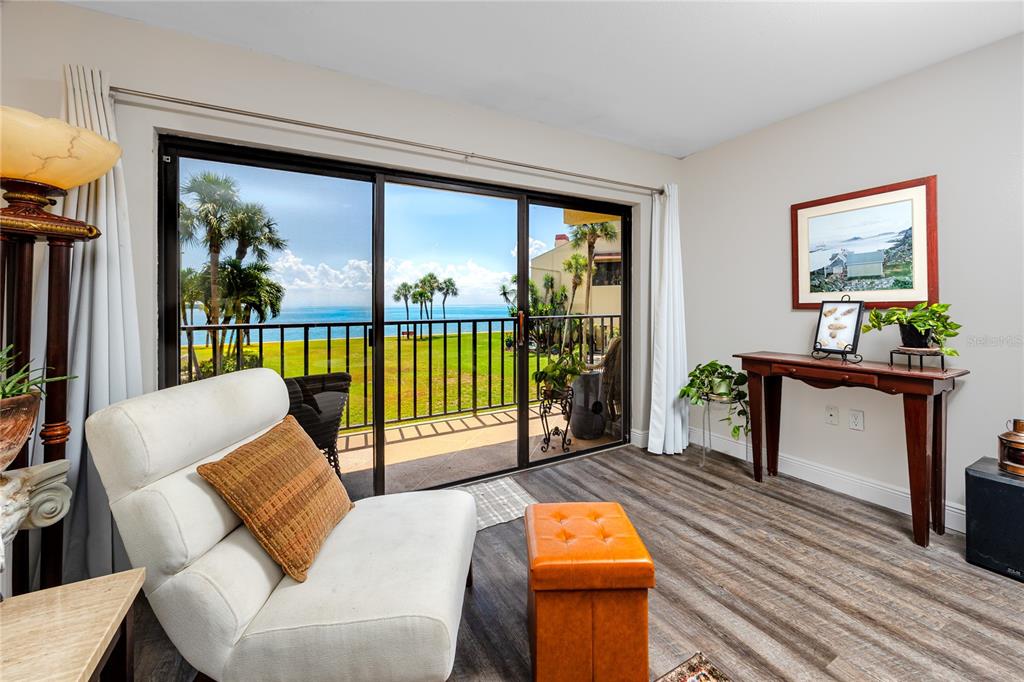 A living room with wood-look flooring, a white chair, and sliding doors overlooking the ocean — 7530 SUNSHINE SKYWAY LANE S UNIT 115, ST PETERSBURG, FL