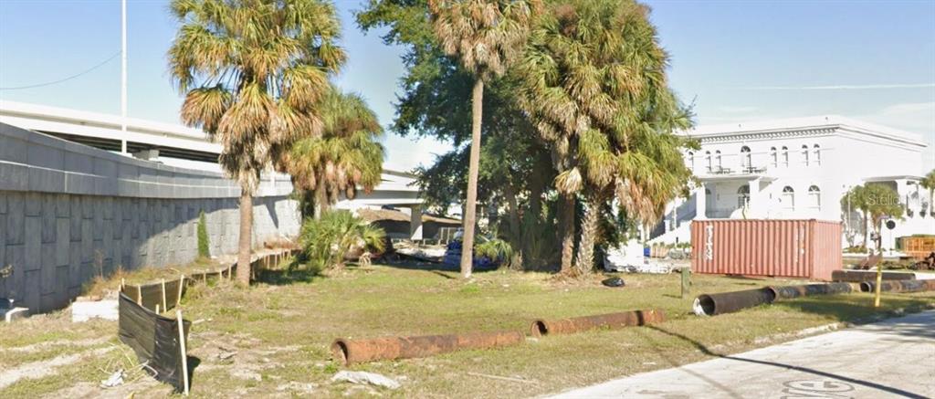 An empty grassy lot sits next to a highway overpass and a white building — 702 E ROSS AVENUE, TAMPA, FL