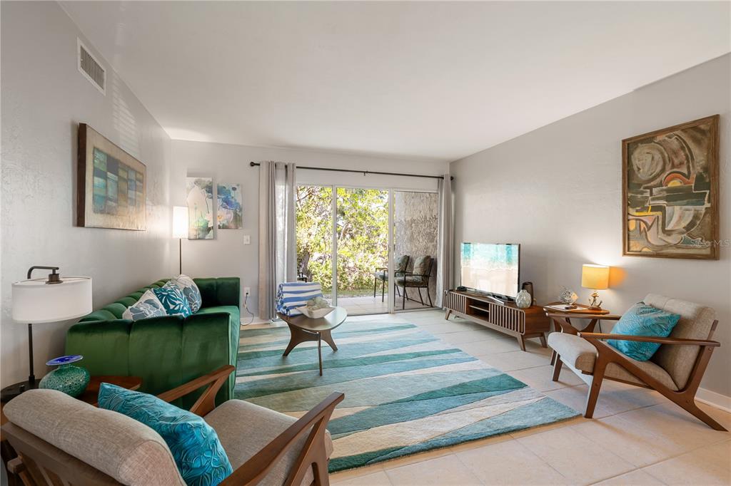 A living room features a green sofa, two armchairs, a patterned rug, and sliding glass doors — 1801 GULF DRIVE N UNIT 148, BRADENTON BEACH, FL