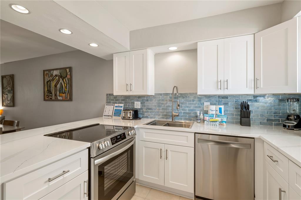A kitchen features white cabinets, stainless steel appliances, and a blue subway tile backsplash — 1801 GULF DRIVE N UNIT 148, BRADENTON BEACH, FL